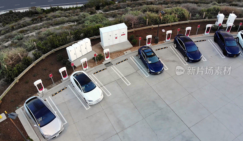 一辆白色特斯拉Model X，一辆白色特斯拉Model S和三辆蓝色特斯拉Model 3停在停车场，在特斯拉超级充电站充电。